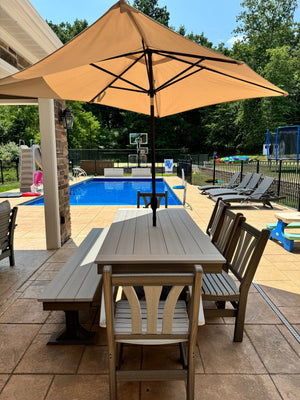 Trestle X Outdoor Bench in weathered gray wood beside a long matching table under a tan umbrella by the pool.