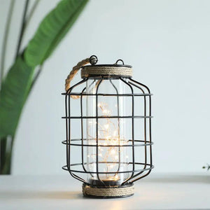 9.4-inch tall battery-powered table lamp with a black metal cage around a glass cylinder and warm string lights