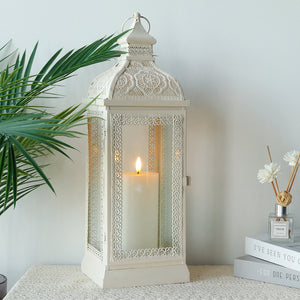 Decorative white metal candle lantern with tempered glass panels and lit candle inside