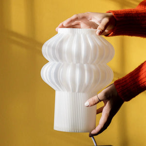 Oppi Table Lamp, white ribbed ceramic, being held against a yellow backdrop