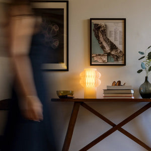 Oppi Table Lamp by Terra Labs, amber ribbed glass base on a wooden table beside stacked books