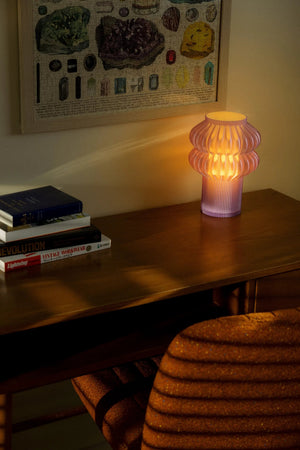 Oppi Table Lamp by Terra Labs; pink ribbed glass lamp casting warm orange glow on wooden desk beside books