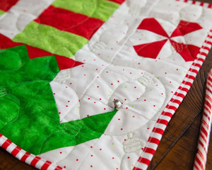 Elf Feet Christmas Table Runner quilt kit; green-red patchwork with white dotted background and striped border.