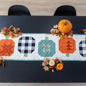 Pumpkin Patchwork Quilted Table Runner Quilt Kit on dark table with pumpkins and autumn leaves