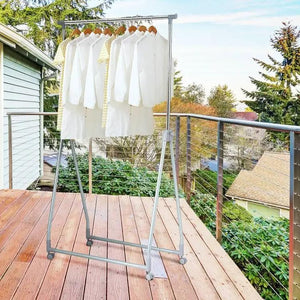 Folding extendable metal garment rack on lockable wheels with hanging rod; several white shirts on a wooden deck.