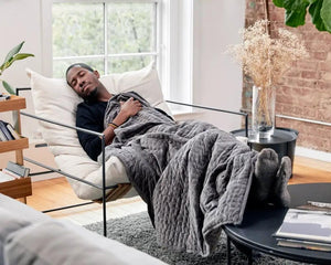 Original Weighted Blanket by Gravity Blankets in gray quilted fabric, draped over a lounge chair with a man resting