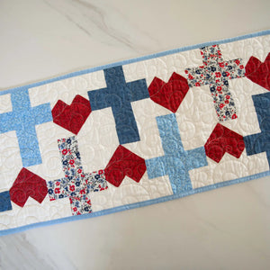 Quilt kit: God Bless America Crosses and Hearts Quilted Table Runner in red, white and blue patchwork with blue binding.
