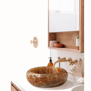 Honey onyx translucent stone vessel sink atop a wooden bathroom vanity with faucet