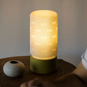 Liunk Table Lamp with a cream ribbed shade and olive-green base on a wooden table.