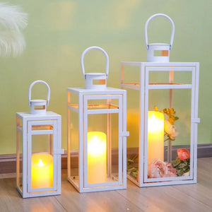 Set of 3 white metal candle lanterns with glass panels and warm amber glow; sizes 12, 15, 19 inches by JHY DESIGN.