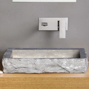 Seagrass Rustic Limestone rectangular bathroom sink above a wood vanity with a square chrome faucet.