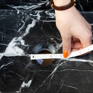 Toros black marble rectangular wall-mount bathroom sink with white veining, measuring tape across the drain opening
