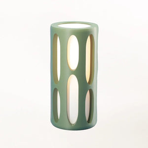 Amoeba Table Lamp by Terra Labs; teal green cylindrical lamp with elongated oval cutouts and warm light.