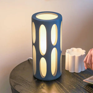 Amoeba Table Lamp, blue cylindrical lamp with vertical oval cutouts emitting warm light