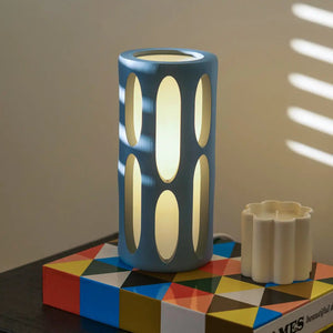 Amoeba table lamp by Terra Labs; blue cylindrical lamp with vertical oval cutouts and a warm glow.
