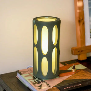 Amoeba Table Lamp by Terra Labs; teal cylindrical lamp with vertical oval cutouts emitting warm yellow light.
