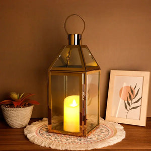 16-inch gold stainless steel candle lantern with glass panes and a lit candle inside
