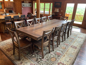 Vineyard-style wooden chairs surround a large rustic dining table in a cabin kitchen.