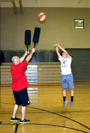 Defender Extender basketball training pads; two black pads held by a man in red, during gym drill with basketball midair.