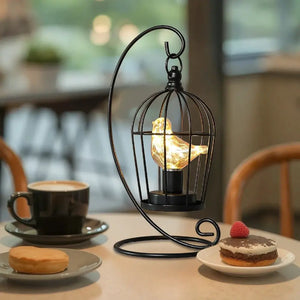 12-inch tall battery-operated birdcage lamp, black metal frame with a warm glowing bird inside on a curved stand.