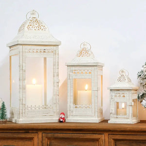 Set of 3 beige vintage metal candle lanterns with glass panels and decorative lattice, candles lit.