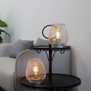 Set of 2 silver metal cage LED lanterns, battery-operated, on a round black side table.