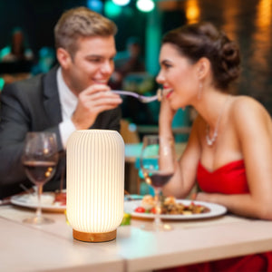 9-inch cylindrical rechargeable lamp with ribbed cream finish on a wooden base, foreground on table.
