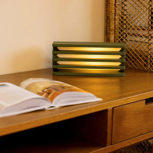 Radiator Table Lamp by Terra Labs in olive green stacked-slat design with warm glow.