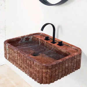 Red travertine wall-mount bathroom sink by Villohome with ribbed textured sides and black faucet