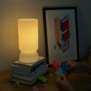 Stance table lamp, ribbed white ceramic, warm glow, on a stack of books