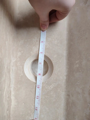 Troia light travertine rustic bathroom sink interior with circular drain and hand-held tape measure