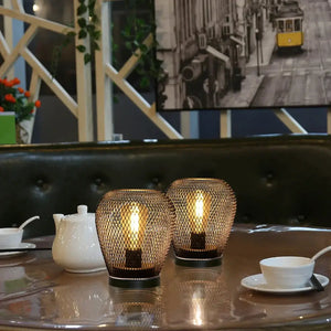 6.7-inch tall battery-powered outdoor table lamp set of 2 on a dining table, bronze mesh cages with warm glow.