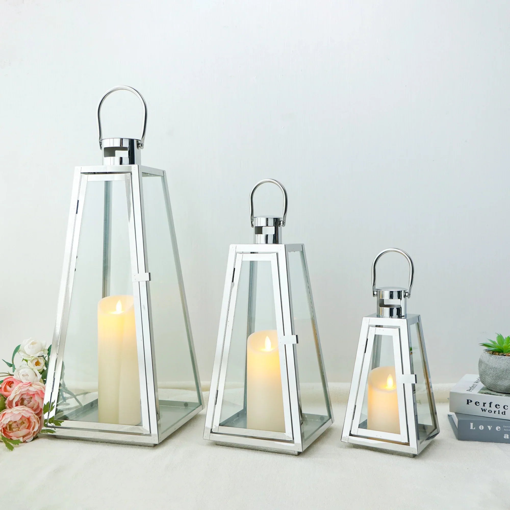Set of decorative glass and metal candle holders with lit candles, displayed in three different sizes on a light surface for a modern home décor look.