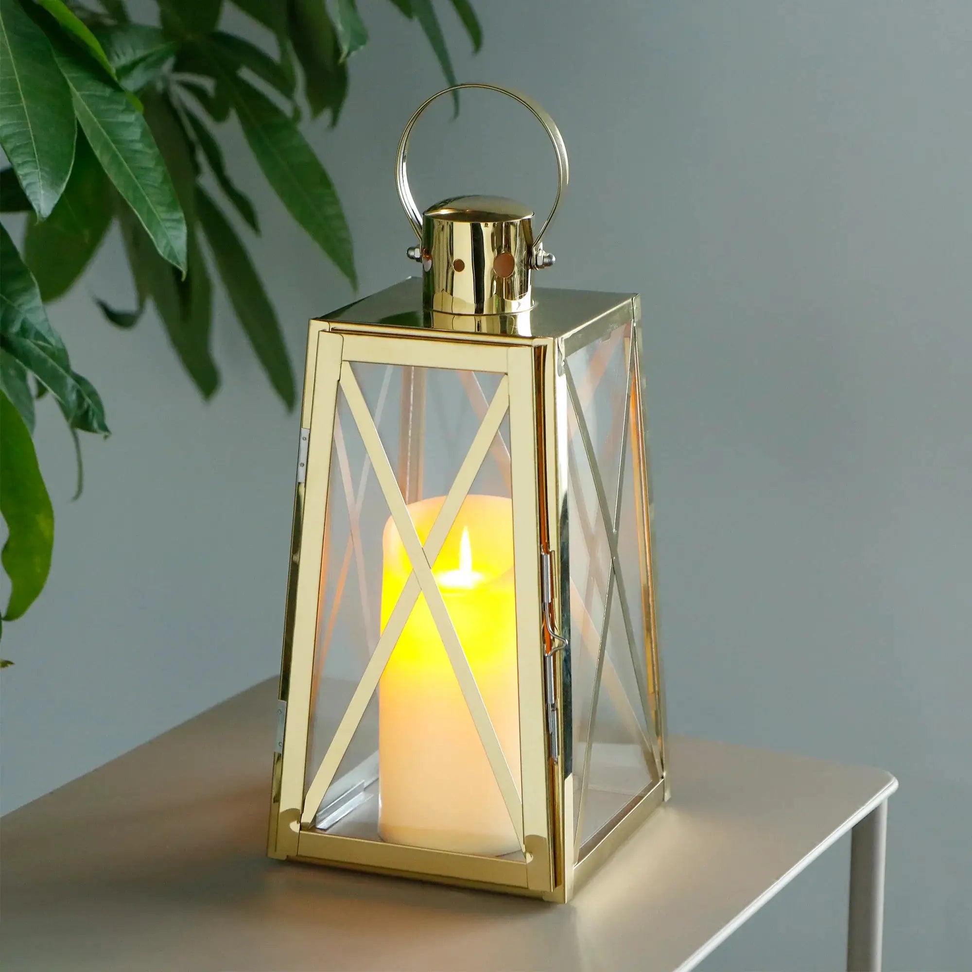 12-inch tall stainless steel decorative lantern, trapezoid with glass panels and gold-tone finish, warm candle glow.
