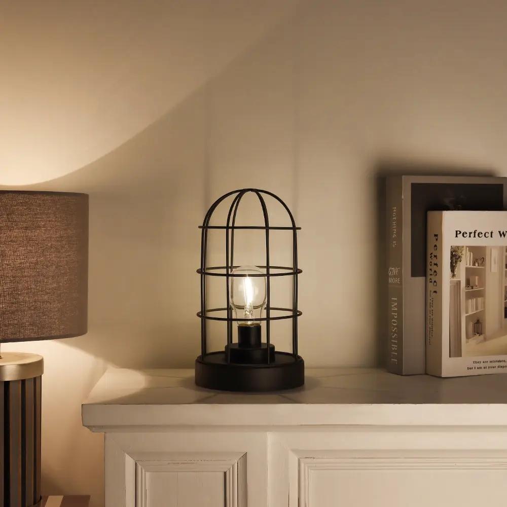 Decorative black metal cage table lamp, cordless with LED bulb, 9.5 inches tall on a mantel.