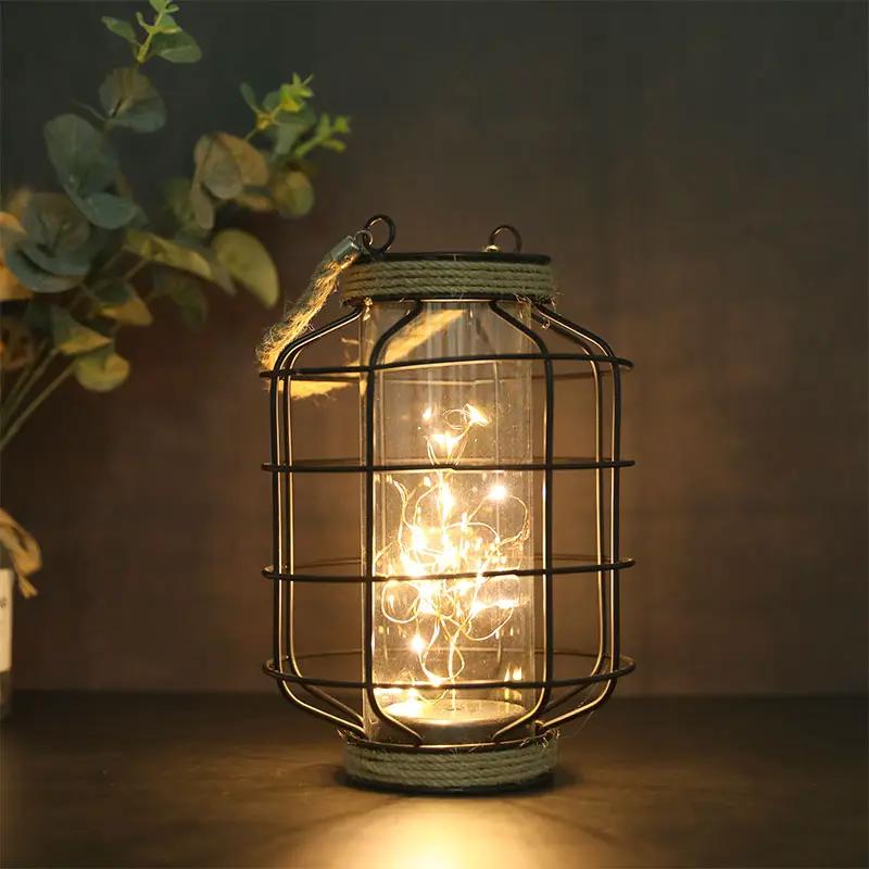 9.4-inch tall battery-powered lantern lamp by JHY DESIGN; glass cylinder with warm LED lights inside, black metal cage