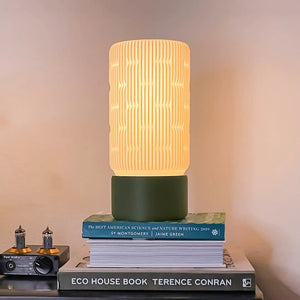Liunk Table Lamp by Terra Labs; cream ribbed shade atop a green base on a stack of books.