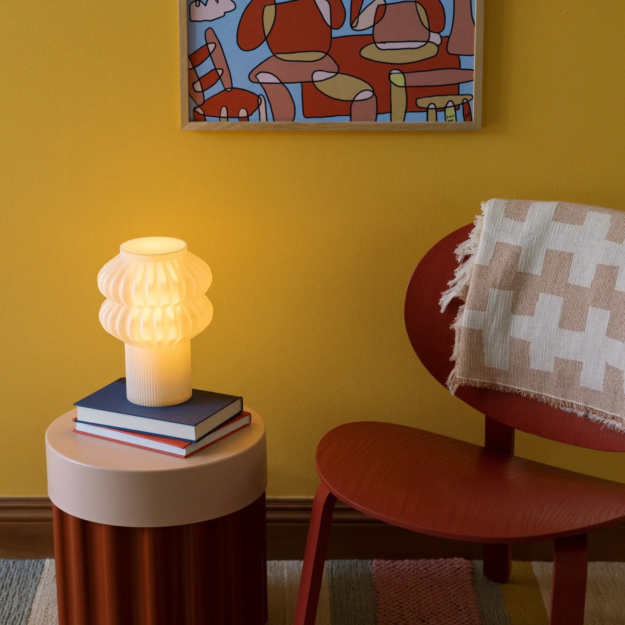 Oppi table lamp by Terra Labs; white ribbed base with pleated shade on a white round table with books.