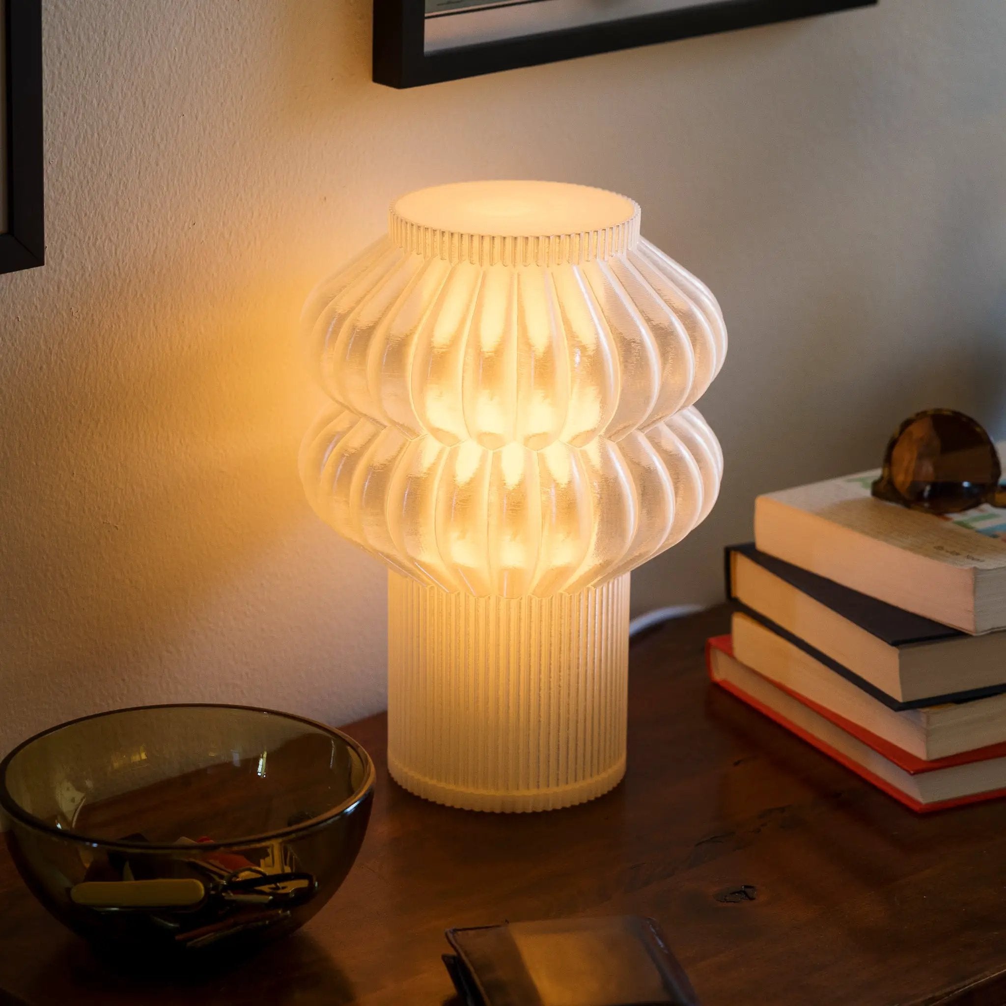 Oppi Table Lamp by Terra Labs in white ribbed ceramic with a warm ambient glow on a desk beside sunglasses.