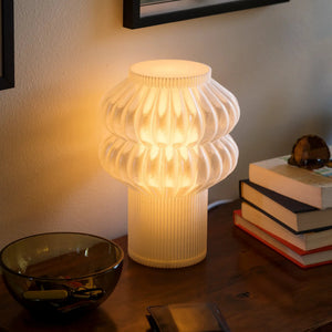 Oppi table lamp by Terra Labs with a ribbed cream glass body and warm glow on a desk.