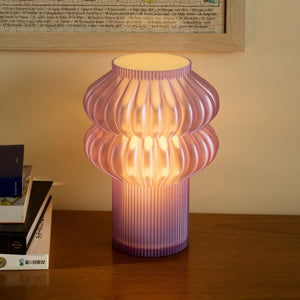 Oppi Table Lamp by Terra Labs; pink ribbed glass lamp with warm glow on wooden surface