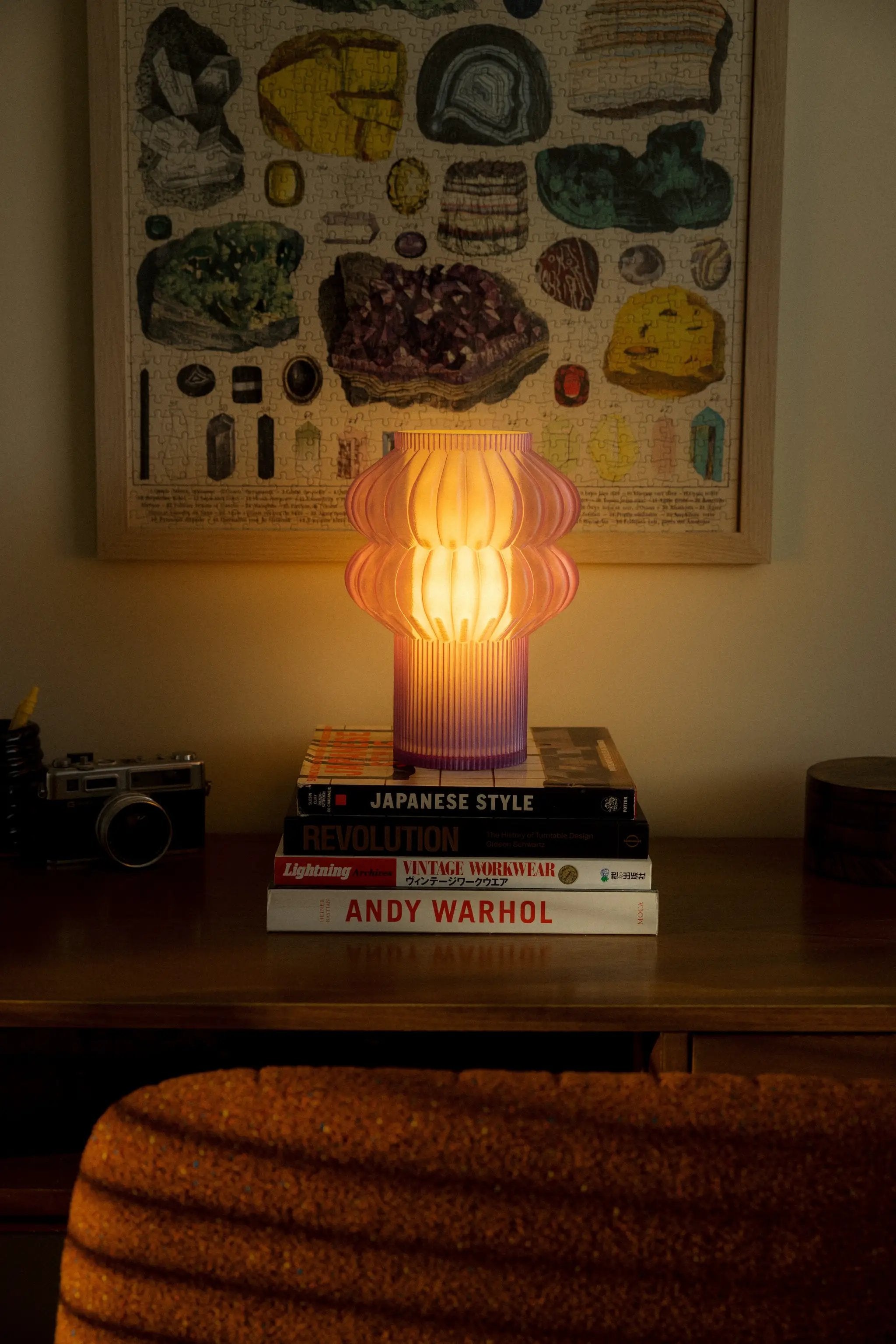Oppi Table Lamp Terra Labs on a stack of design books, pink ribbed glass with a warm glow