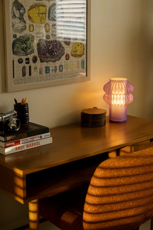 Oppi table lamp by Terra Labs, pink ribbed glass on a wooden desk beside framed artwork.
