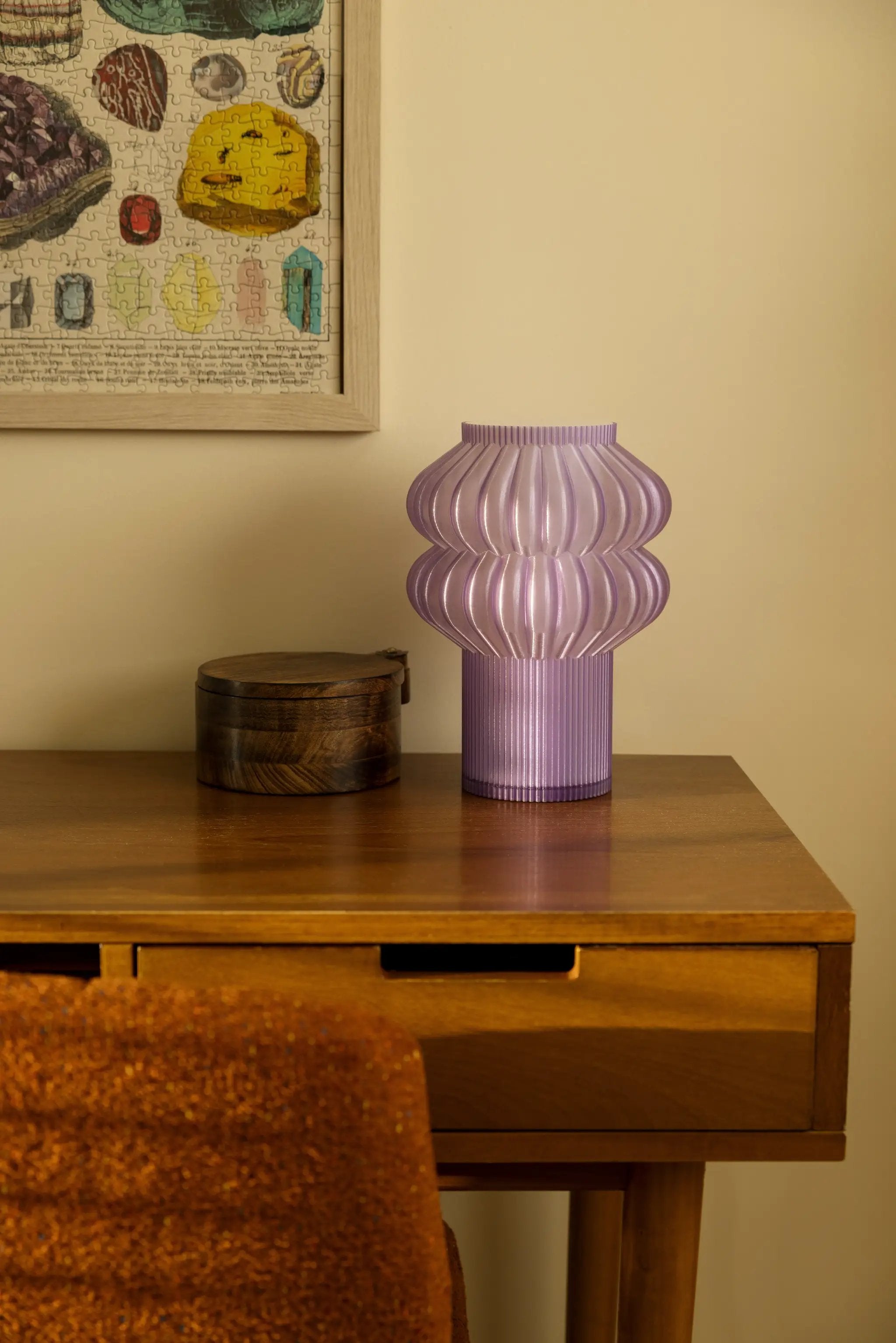 Oppi Table Lamp; purple ribbed lamp on a wooden desk beside a framed puzzle.