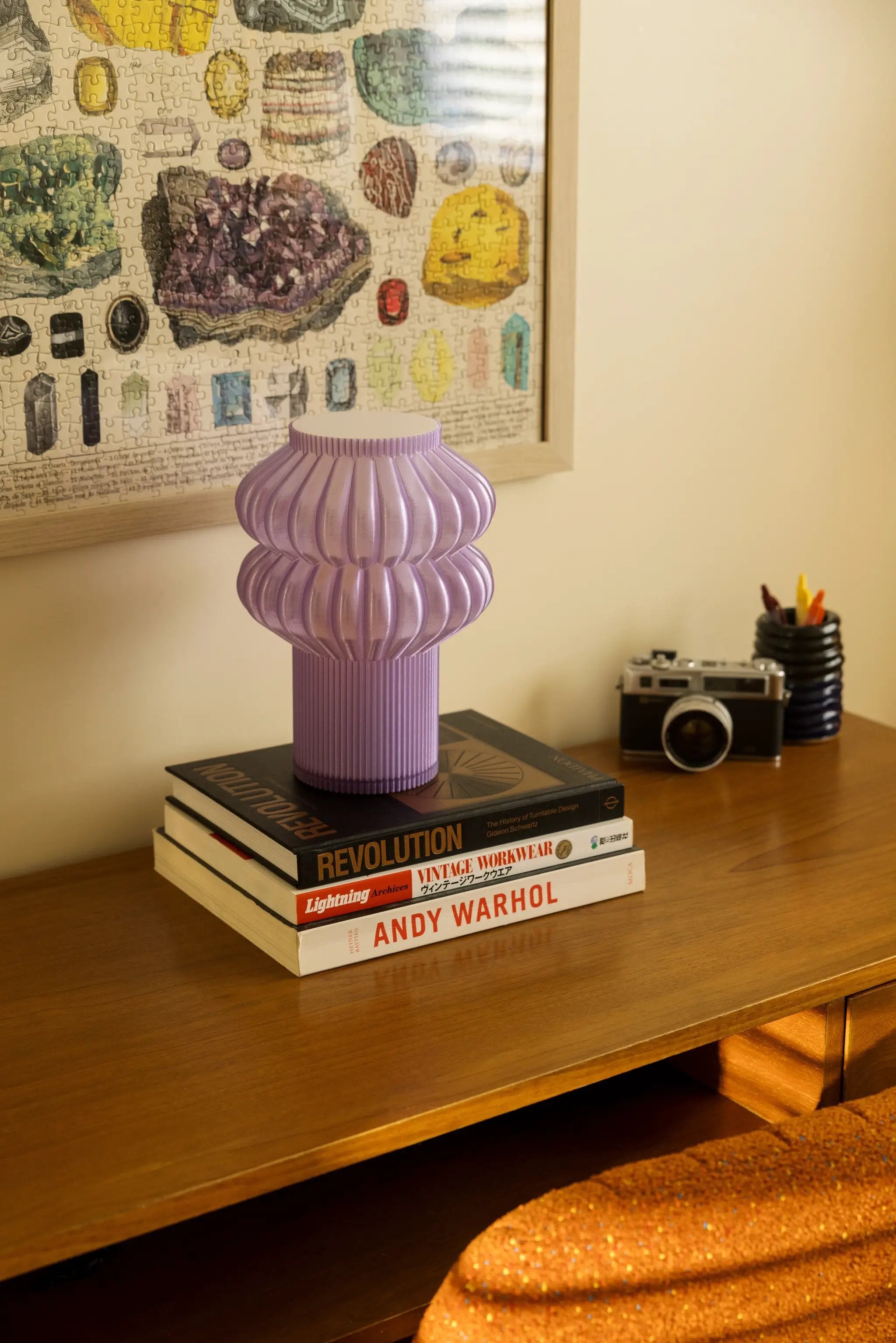 Oppi Table Lamp, purple ribbed base atop a stack of design books on a wooden desk