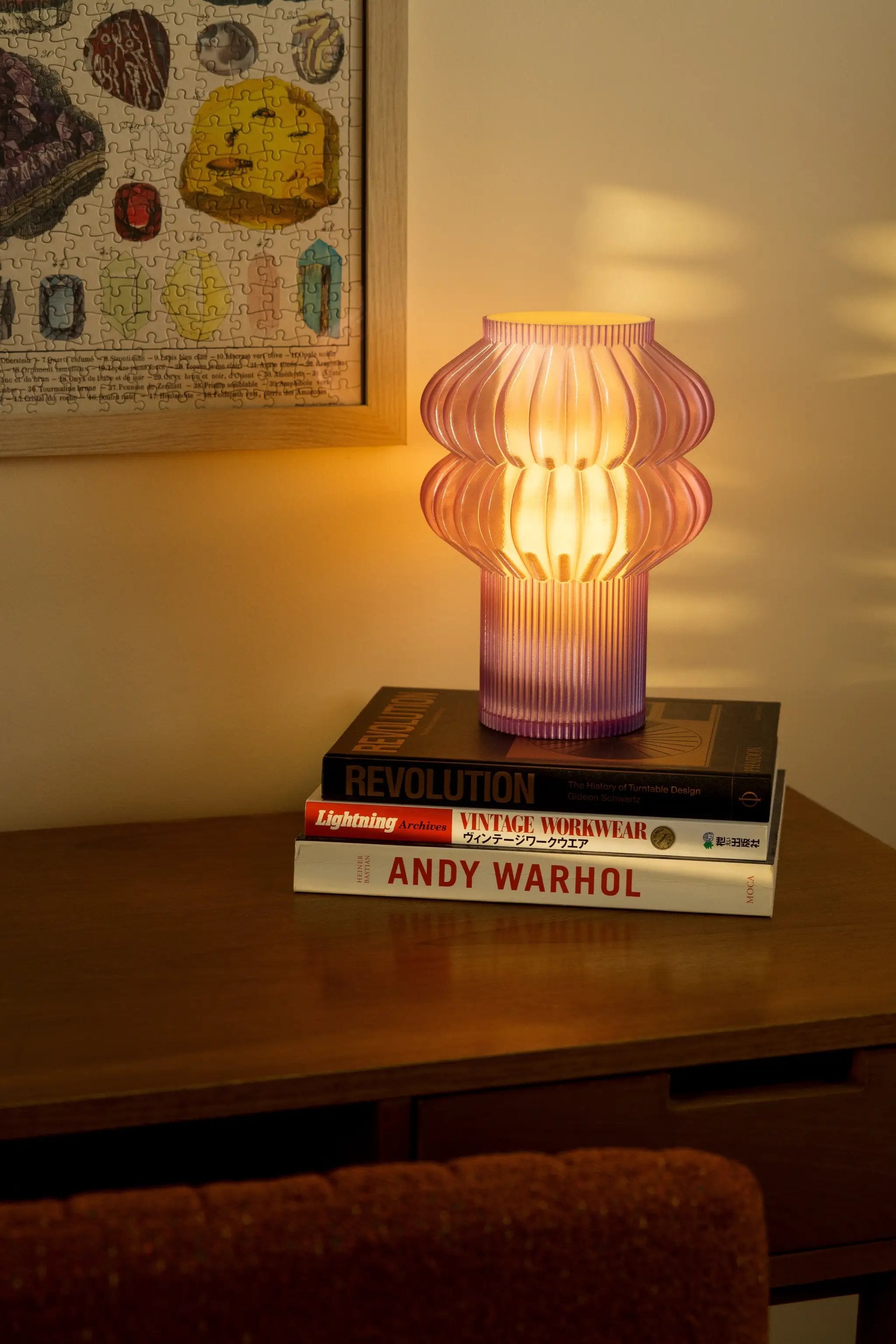 Oppi table lamp by Terra Labs; pink ribbed glass lamp glowing warmly on a stack of design books.