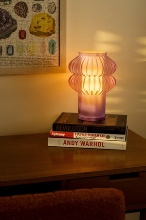 Oppi table lamp by Terra Labs; pink ribbed glass lamp glowing warmly on a stack of design books.
