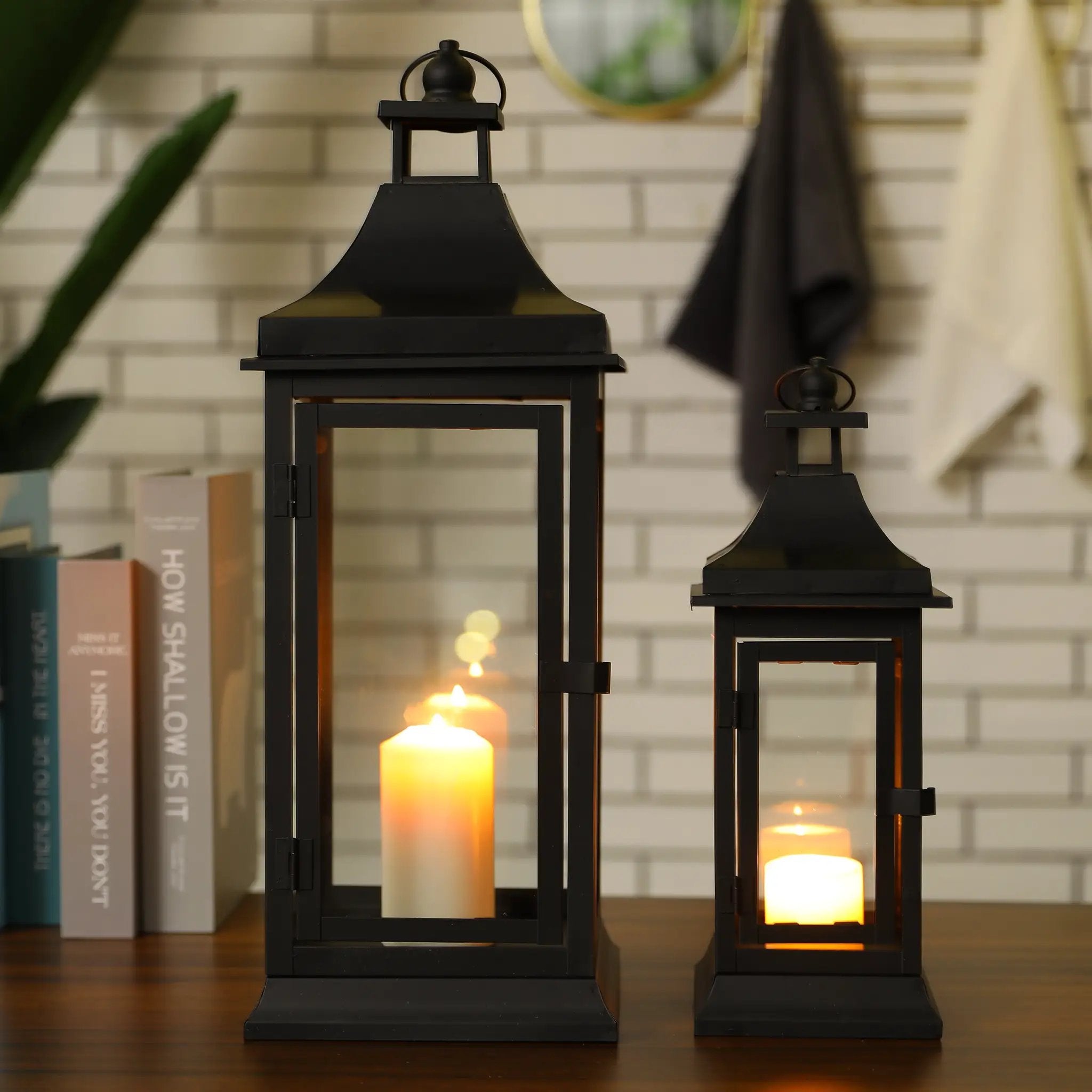 Set of 2 black outdoor candle lanterns, 13 and 19.5 inches tall, with glass panels and warm glowing candles.