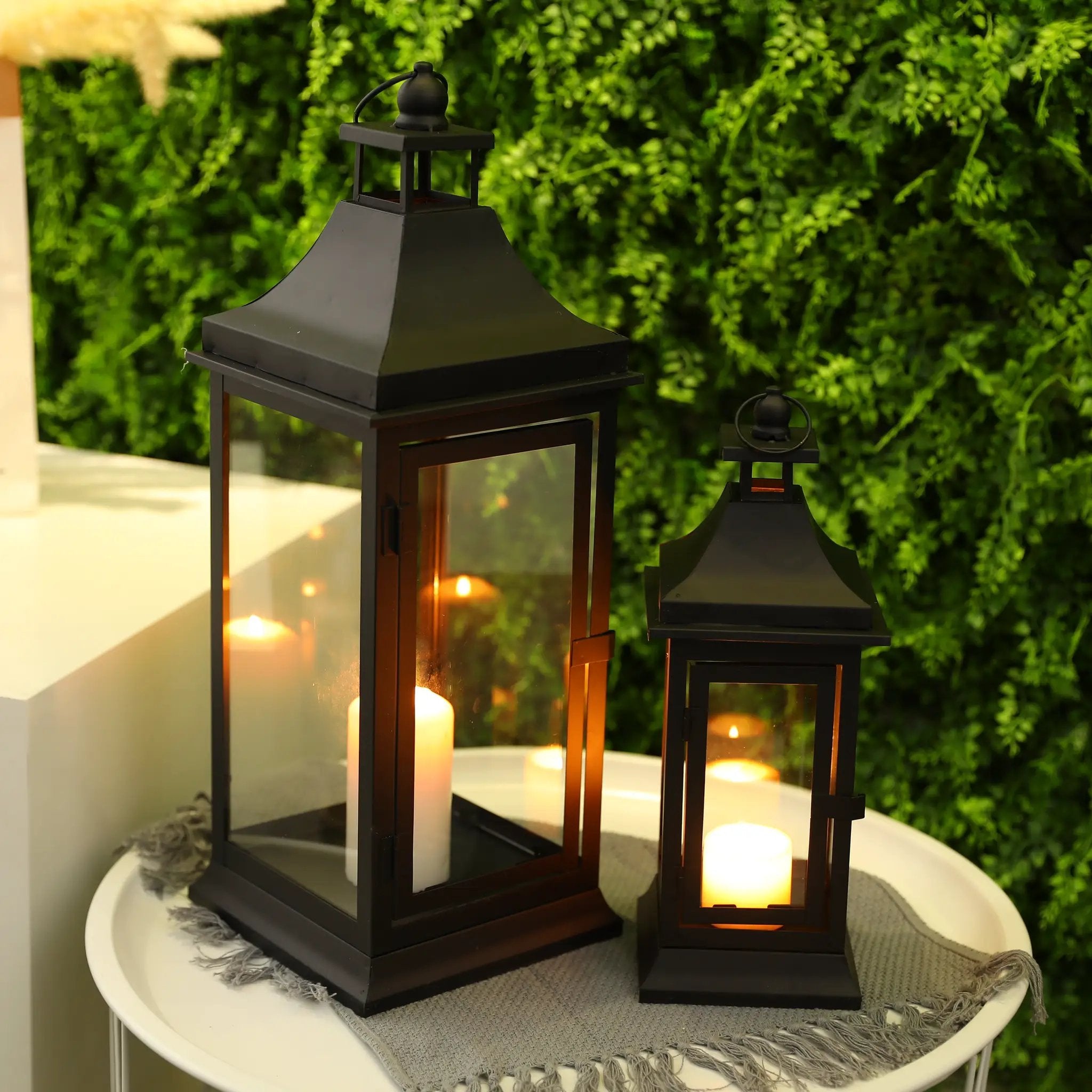 Set of 2 outdoor candle lanterns, 13in and 19.5in tall, black metal with glass panels and glowing candles