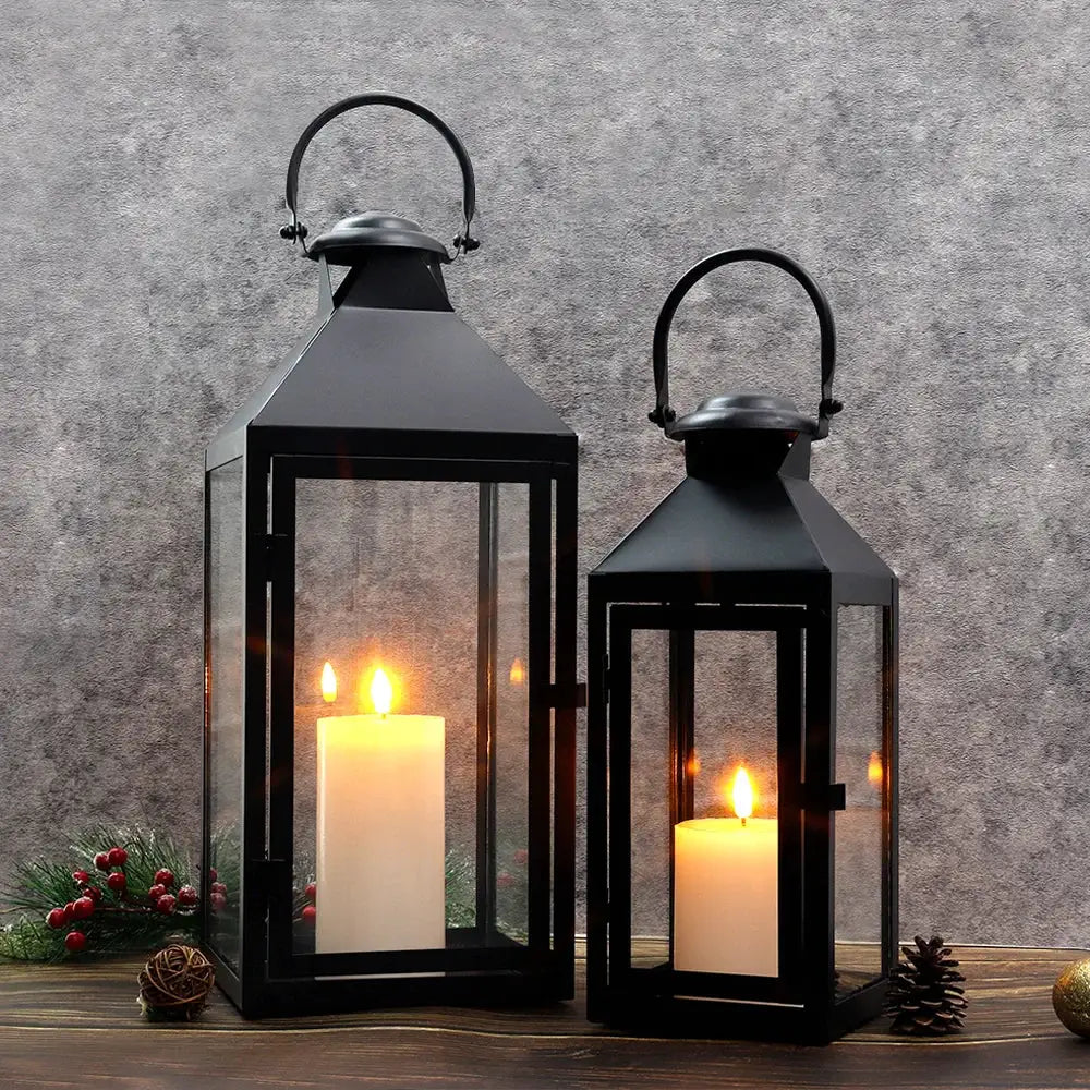 Set of 2 high black metal candle lanterns with glass panels and warm lit candles.